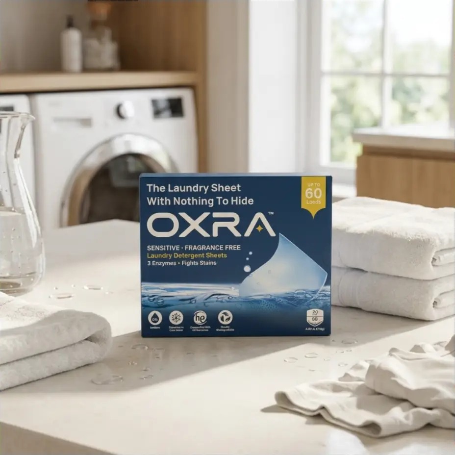 OXRA laundry detergent sheets box on a kitchen counter beside a washing machine and folded towels